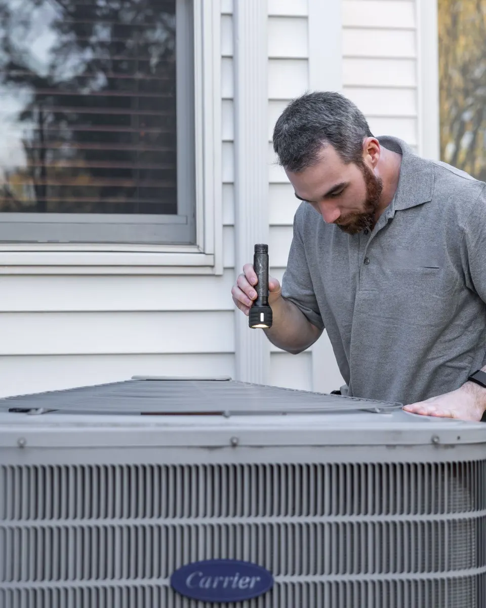 A heating and air technician inspecting an outdoor unit