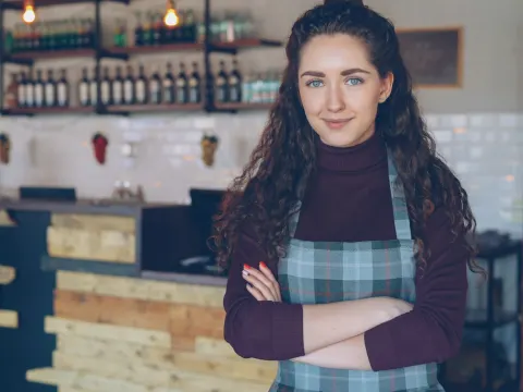 Cafe owner with arms crossed inside a cozy coffee shop