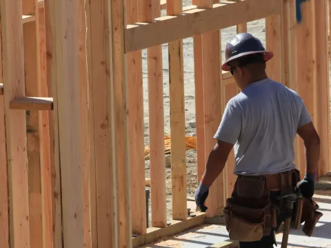 Builder in a hard hat and tool belt framing a house